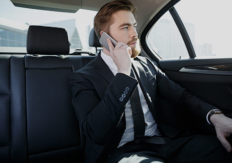 Homme au téléphone en costume assis à l'arrière d'un véhicule avec chauffeur