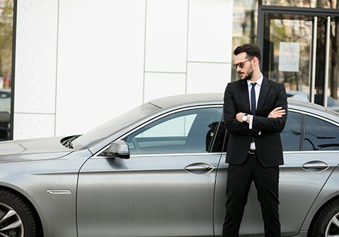 Jaune homme en costume attendant les bras croisés devant un véhicule de luxe