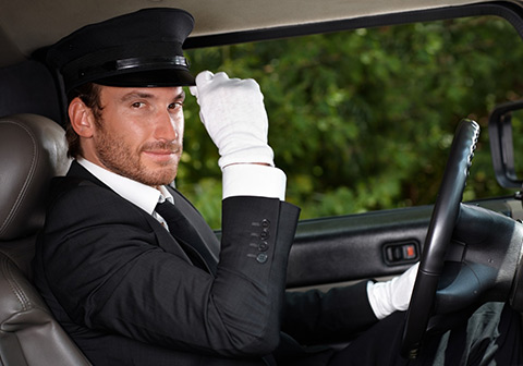 Prestation véhicules avec chauffeur, homme souriant en costume conduisant une limousine.